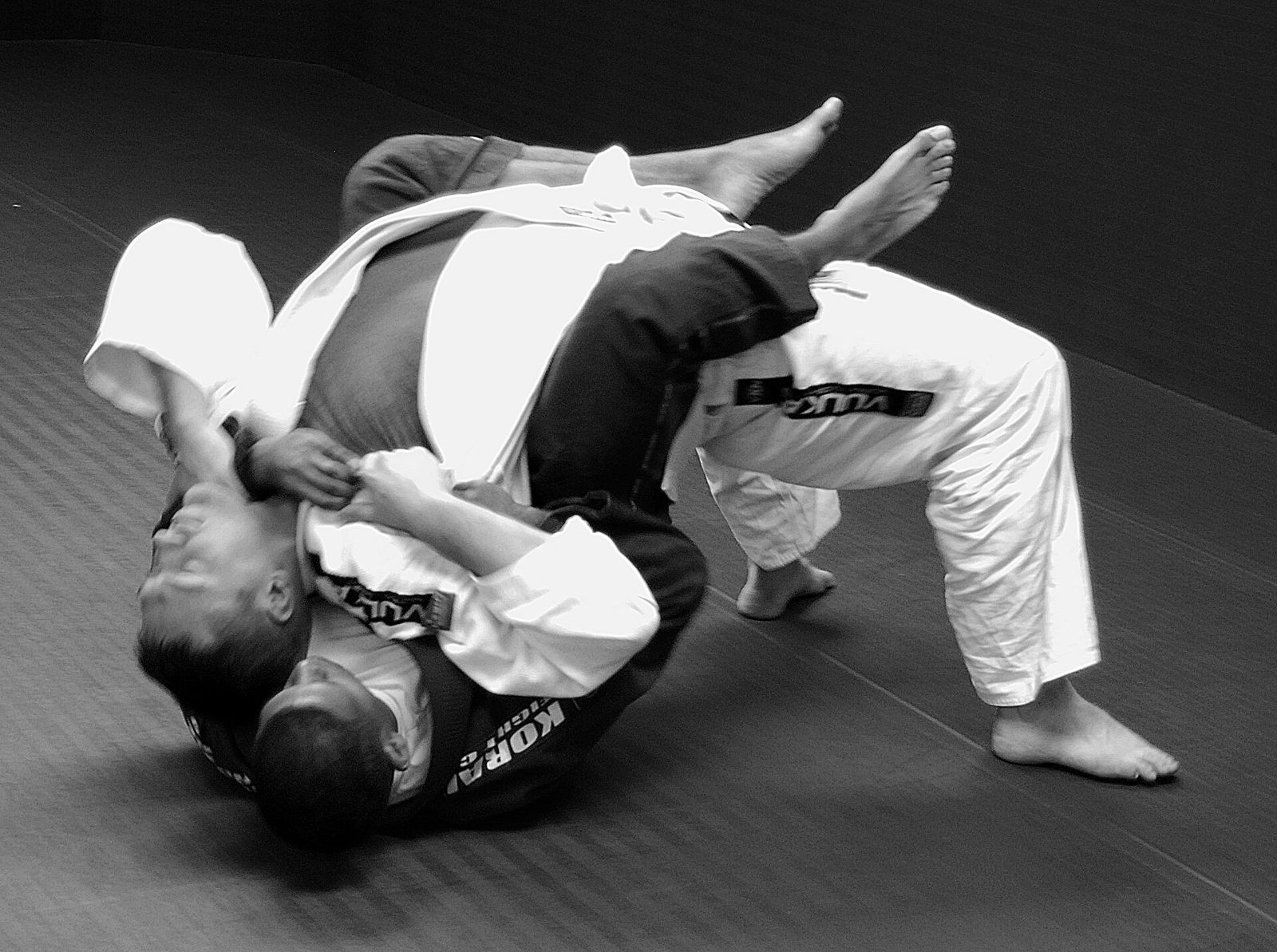 Photo noir et blanc : un pratiquant de ju-jitsu brésilien prend le dos de son partenaire au sol