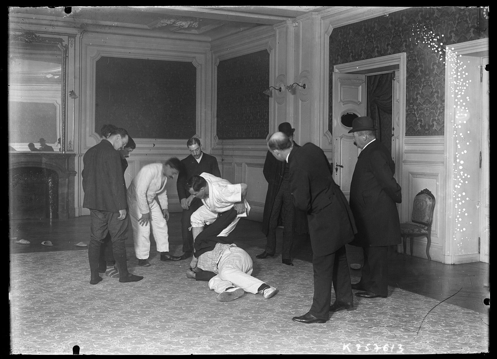 Photo d'archive, 1905 : démonstration de jiu-jitsu devant des hommes en costume, dans un salon parisien