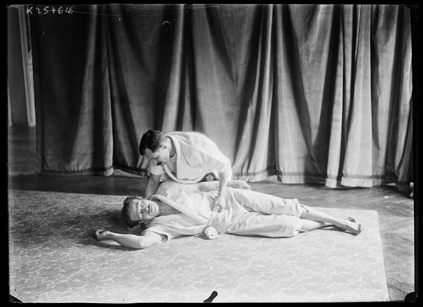 Photo d'archive, 1905 : un pratiquant de jiu-jitsu immobilise son partenaire au sol devant un rideau